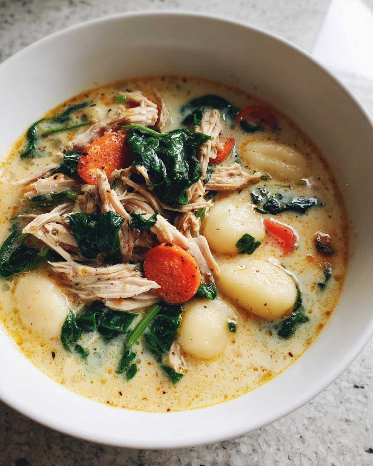 Close-up of a creamy bowl of Olive Garden Chicken Gnocchi Soup featuring shredded chicken, spinach, carrots, and soft gnocchi.