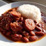 A plate of flavorful beans and rice topped with thick slices of smoked sausage.