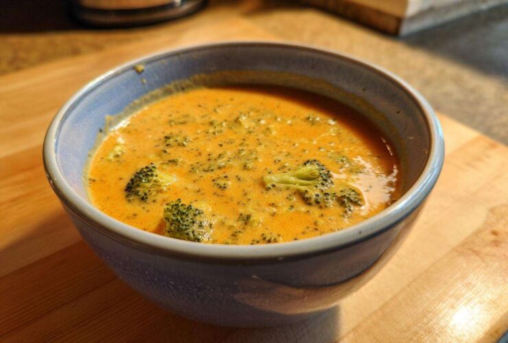 Close-up of a bowl of rich, orange broccoli cheddar soup with visible pieces of broccoli florets.