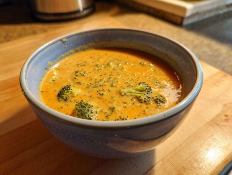 Close-up of a bowl of rich, orange broccoli cheddar soup with visible pieces of broccoli florets.