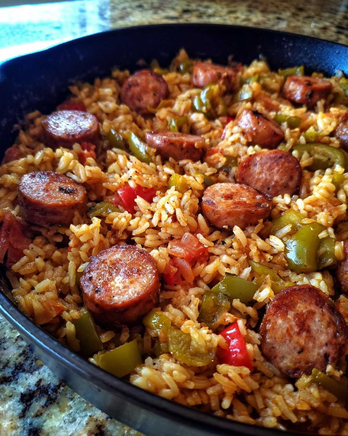 Close-up of flavorful one-pot sausage and rice cooked with green peppers and tomatoes in a dark skillet.