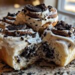 A close-up shot of several gooey Oreo cinnamon rolls topped with thick white frosting and crushed Oreo pieces.