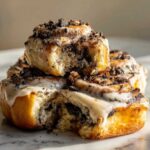 A stack of gooey Oreo cinnamon rolls covered in white icing and crushed cookie pieces.