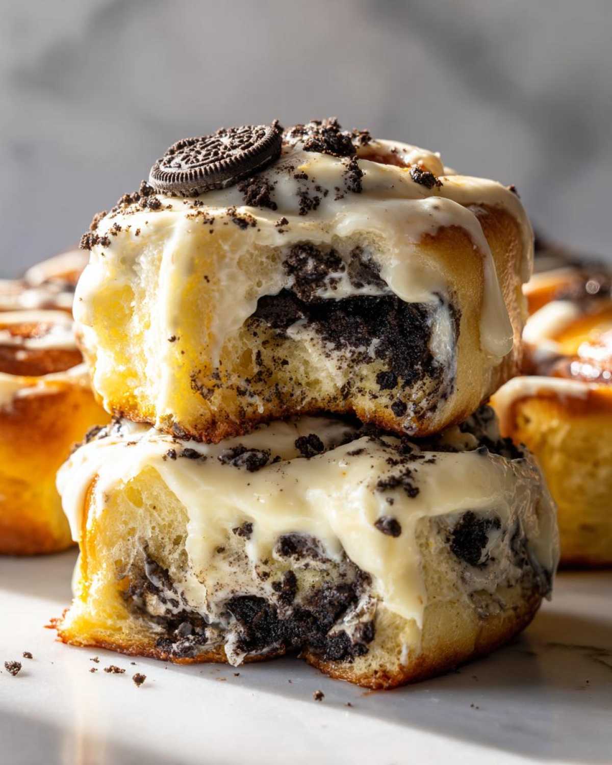 Two stacked, gooey Oreo cinnamon rolls covered in white icing and crushed Oreo pieces.