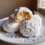 A stack of delicious Russian tea cakes heavily dusted with powdered sugar, one cookie is broken open showing the nutty interior.
