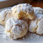 A close-up of several delicious Russian tea cakes heavily dusted with powdered sugar on a white plate.