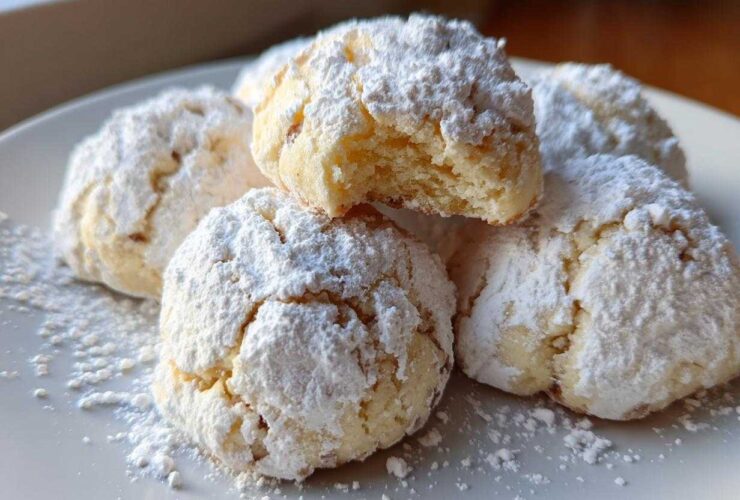 A close-up of several delicious Russian tea cakes heavily dusted with powdered sugar on a white plate.