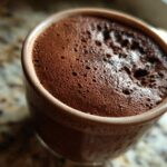 Close-up overhead view of rich, dark chocolate mousse with fine bubbles in a small brown cup.