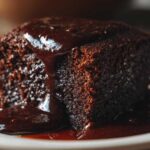 A close-up of a moist slice of chocolate pudding cake drenched in dark chocolate sauce.
