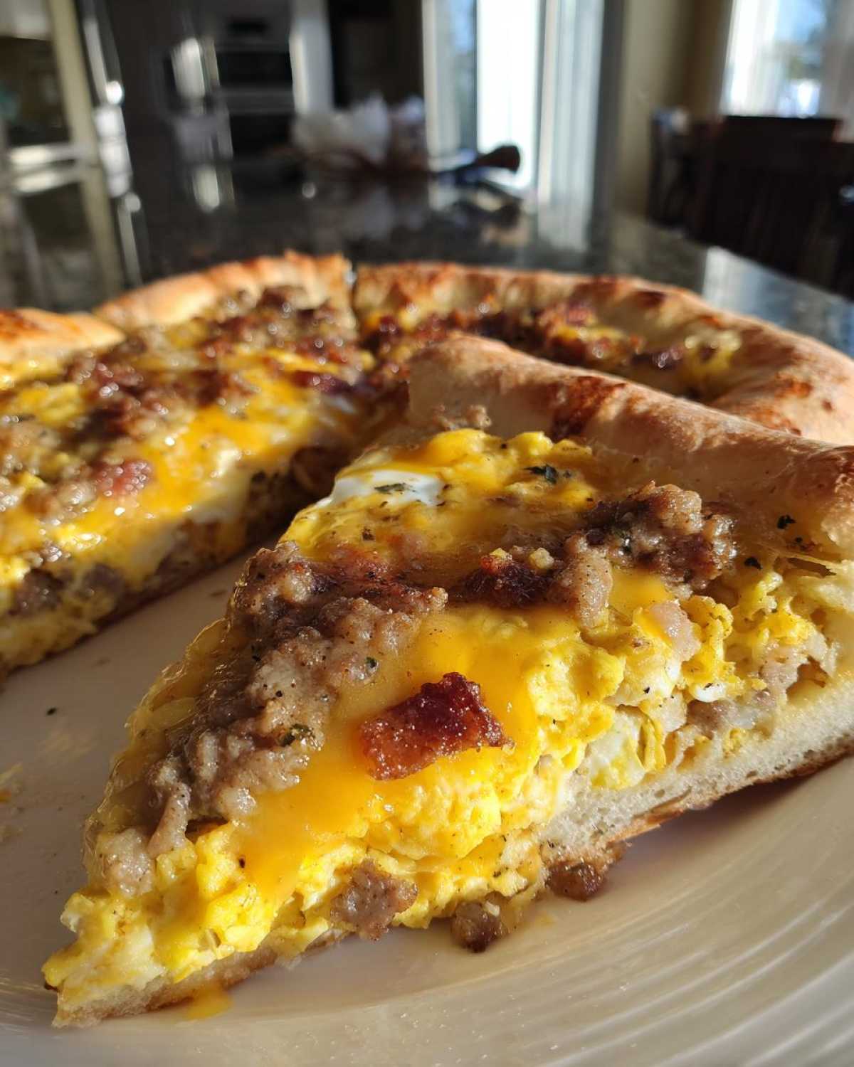 Close-up of a thick slice of sausage gravy breakfast pizza showing scrambled eggs, crumbled sausage, and melted cheddar cheese.