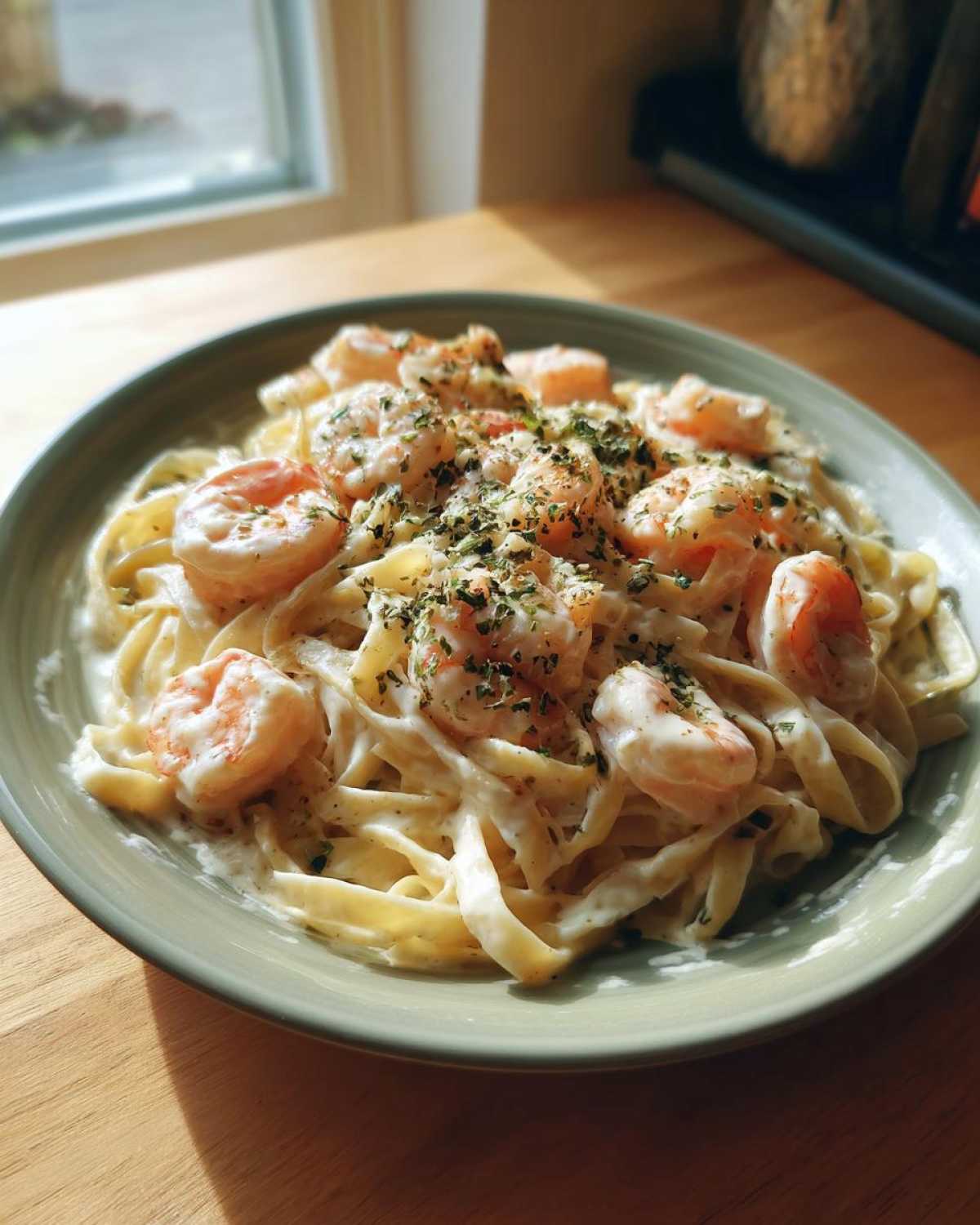 A close-up of a plate of shrimp alfredo pasta topped generously with dried herbs.