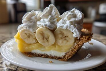 A decadent slice of banana cream pie recipe featuring a graham cracker crust, creamy filling, sliced bananas, and whipped cream.