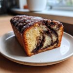 A close-up of a slice of moist chocolate babka bread, featuring a beautiful swirl pattern and topped with a shiny chocolate glaze.