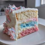 A slice of multi-layered cotton candy cake showing pink, blue, and white sponge layers with white frosting and pastel swirls.