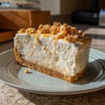 A thick slice of creamy white christmas tree cheesecake with a graham cracker crust, drizzled with caramel and topped with crumbles.
