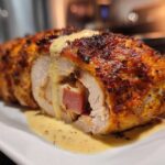 A close-up view of sliced chicken cordon bleu, showing ham and cheese filling, topped with a creamy sauce.