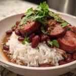 A close-up of a bowl filled with white rice, topped with red beans, sliced sausage, and fresh parsley for slow cooker red beans and rice.