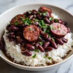 A close-up of a bowl of slow cooker red beans and rice topped with sliced andouille sausage and fresh parsley.