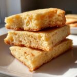 Three thick, square-cut sugar cookies stacked on a white plate, showing their soft, buttery texture.