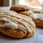 A close-up of several soft maple cookies topped with a zigzag drizzle of white icing, sitting on a white plate.