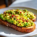 Two slices of perfectly toasted bread topped with mashed avocado and sprinkled generously with red pepper flakes, classic avocado toast.