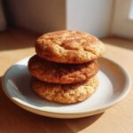 Three soft, thick applesauce cookies stacked on a speckled white plate, coated in cinnamon sugar.