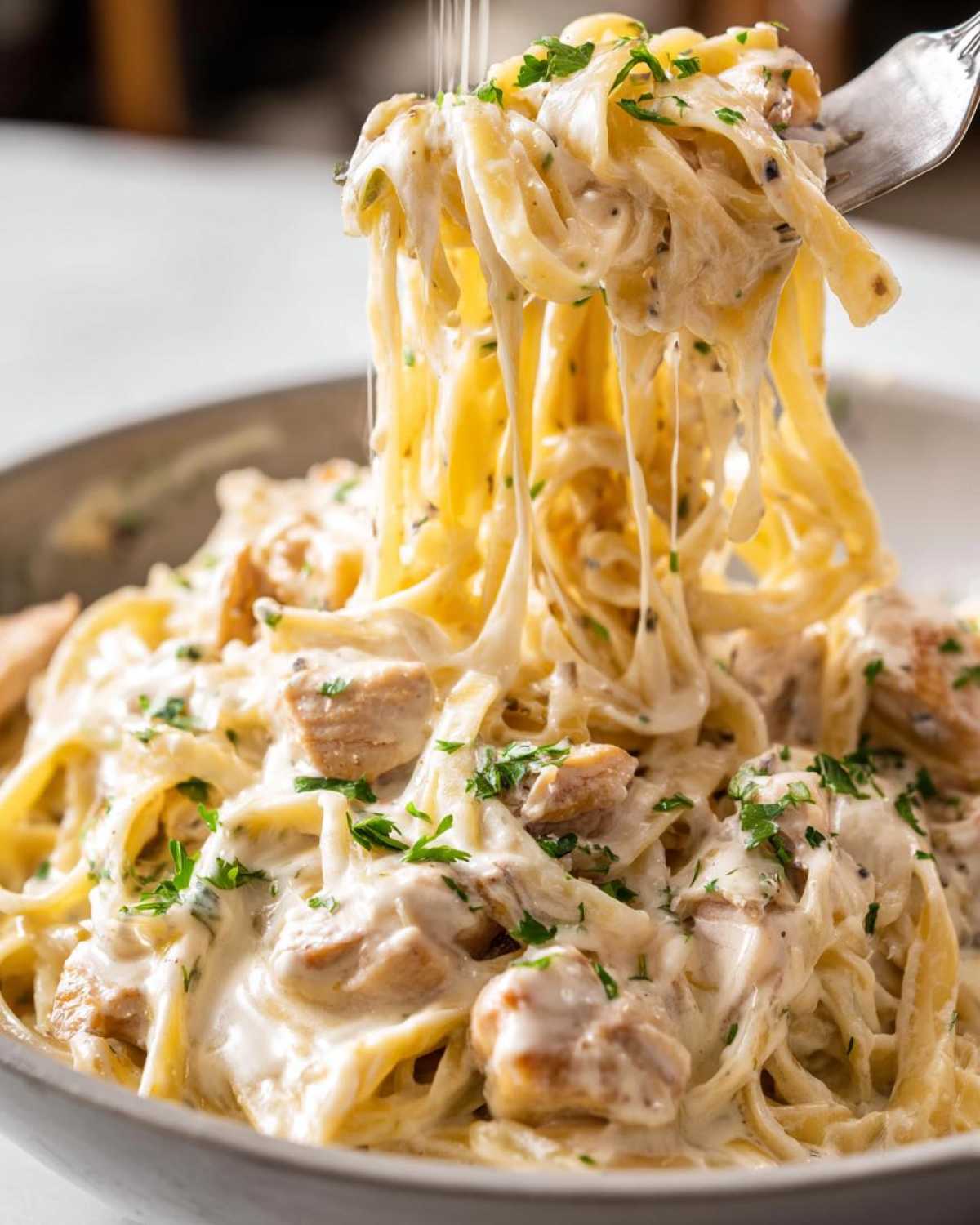 A fork lifting fettuccine noodles covered in creamy sauce and chicken pieces from a bowl of chicken alfredo.