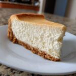 A close-up of a thick, creamy slice of sugar cookie cheesecake with a golden-brown crust.
