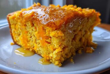 Close-up of a moist slice of bright orange sweet potato cornbread drizzled generously with golden honey.