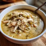 Close-up of a white bowl filled with creamy white chicken chili, featuring shredded chicken, white beans, and green chilies.