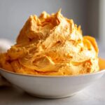 A close-up of vibrant orange pumpkin fluff, whipped and piled high in a simple white bowl.