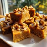Close-up of rich, brown maple fudge squares topped with chopped walnuts on a white plate.