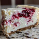 Close-up of a creamy slice of white chocolate cheesecake featuring a vibrant raspberry swirl topping and graham cracker crust.