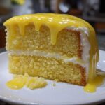 A moist slice of yellow layer cake topped with thick, dripping lemon glaze, part of a lemon cake recipe.