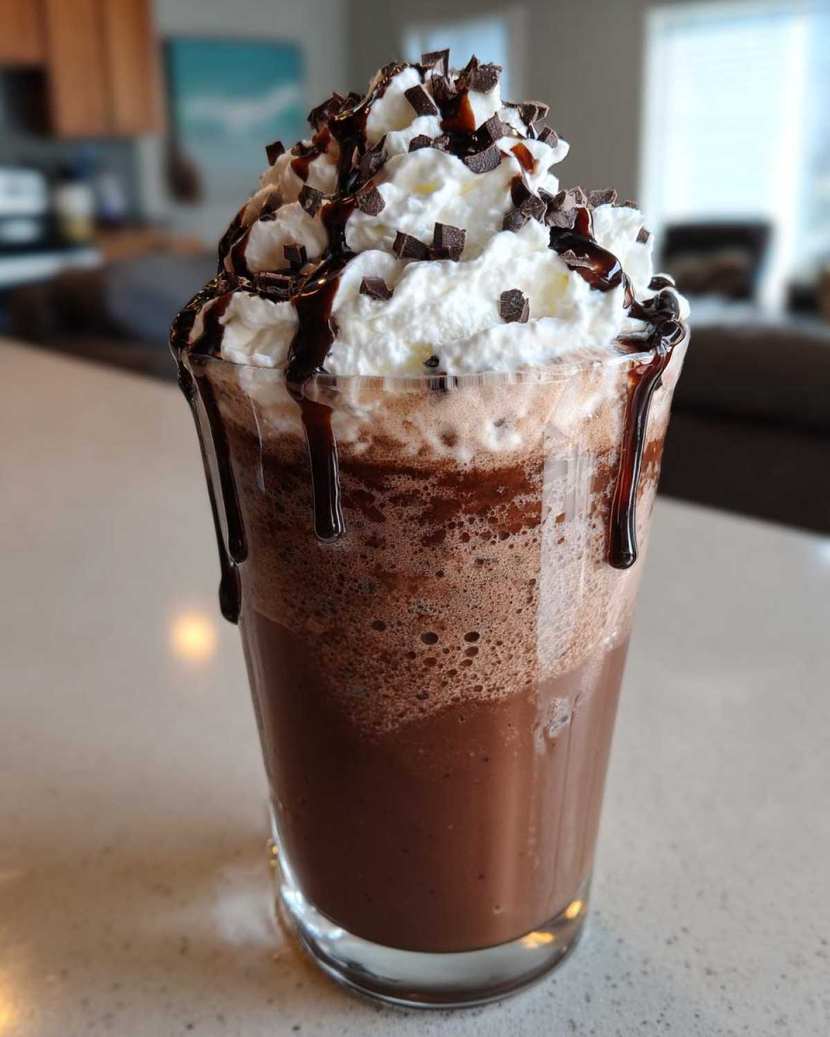 A tall glass filled with rich, blended frozen hot chocolate topped with whipped cream, chocolate syrup, and shavings.