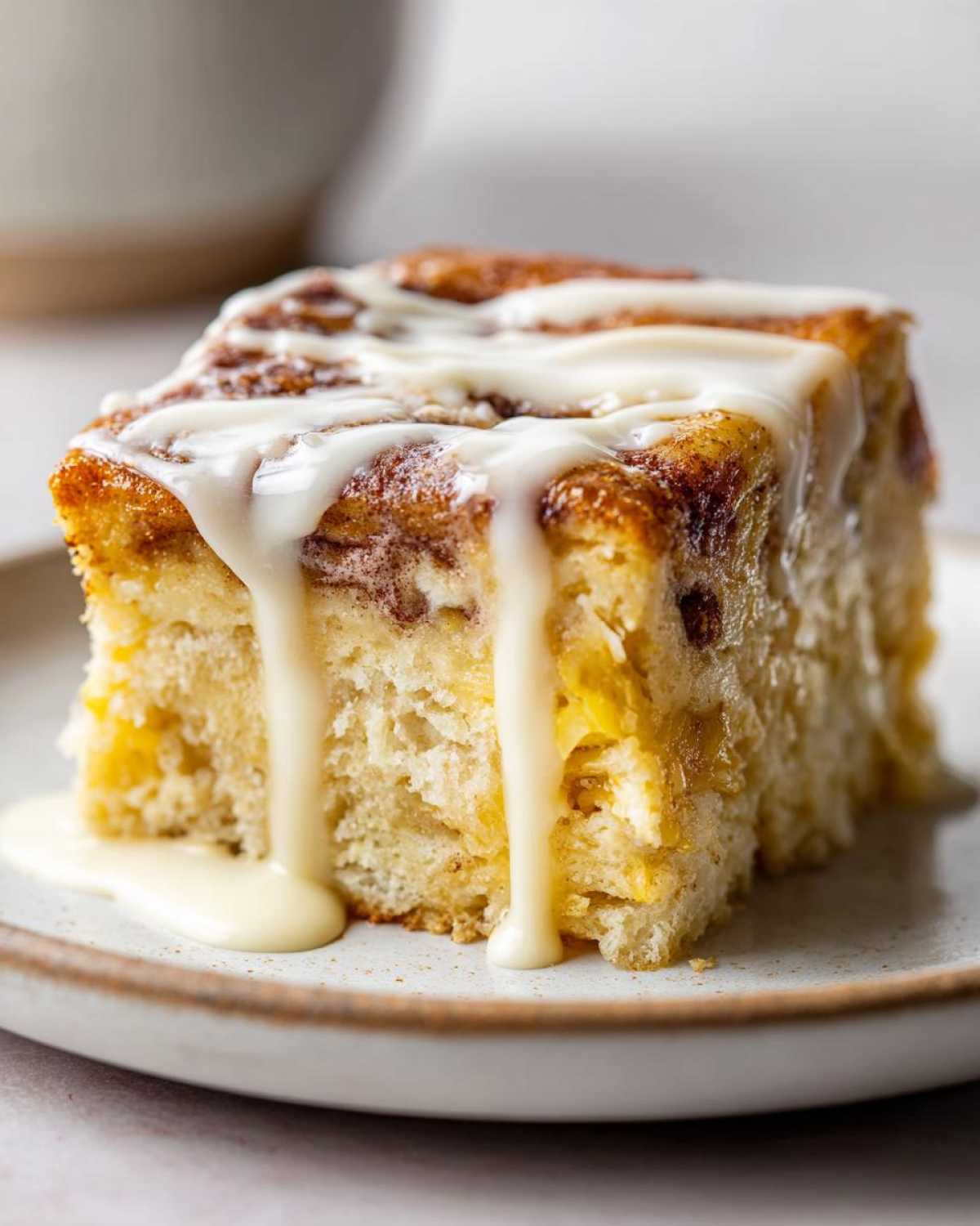 Close-up of a square slice of fluffy cinnamon roll casserole topped with thick white icing dripping down the sides.