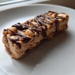 Close-up of a homemade protein bar topped with peanuts and drizzled with dark chocolate.