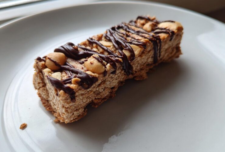 Close-up of a homemade protein bar topped with peanuts and drizzled with dark chocolate.