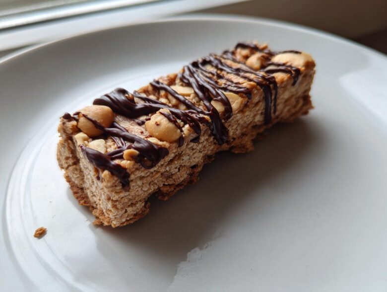 Close-up of a homemade protein bar topped with peanuts and drizzled with dark chocolate.