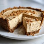 A creamy slice of no-bake peanut butter pie with a thick graham cracker crust, served on a white plate.