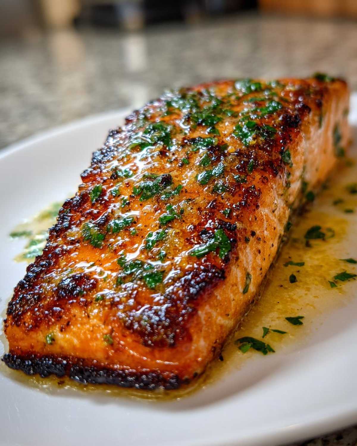Close-up of a glistening, perfectly cooked air fryer salmon fillet topped with melted butter and fresh parsley.