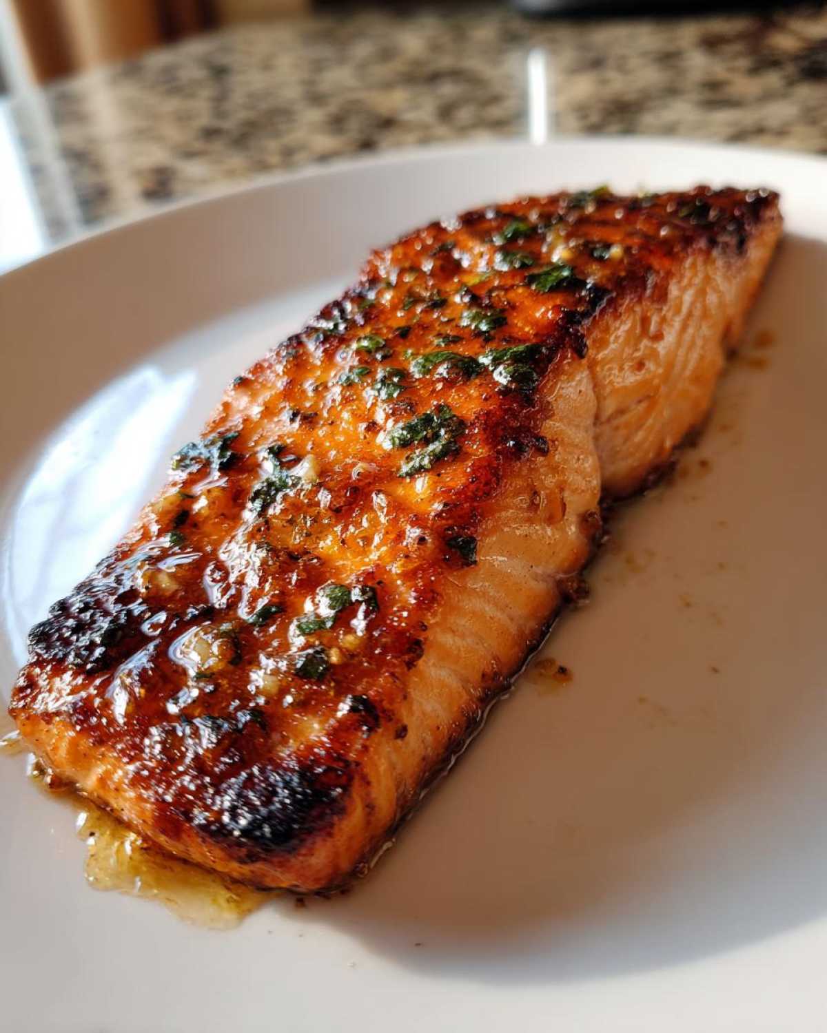 A perfectly cooked, glazed air fryer salmon fillet topped with herbs, resting on a white plate.
