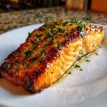 Close-up of a glistening, perfectly cooked piece of air fryer salmon topped with chopped parsley.