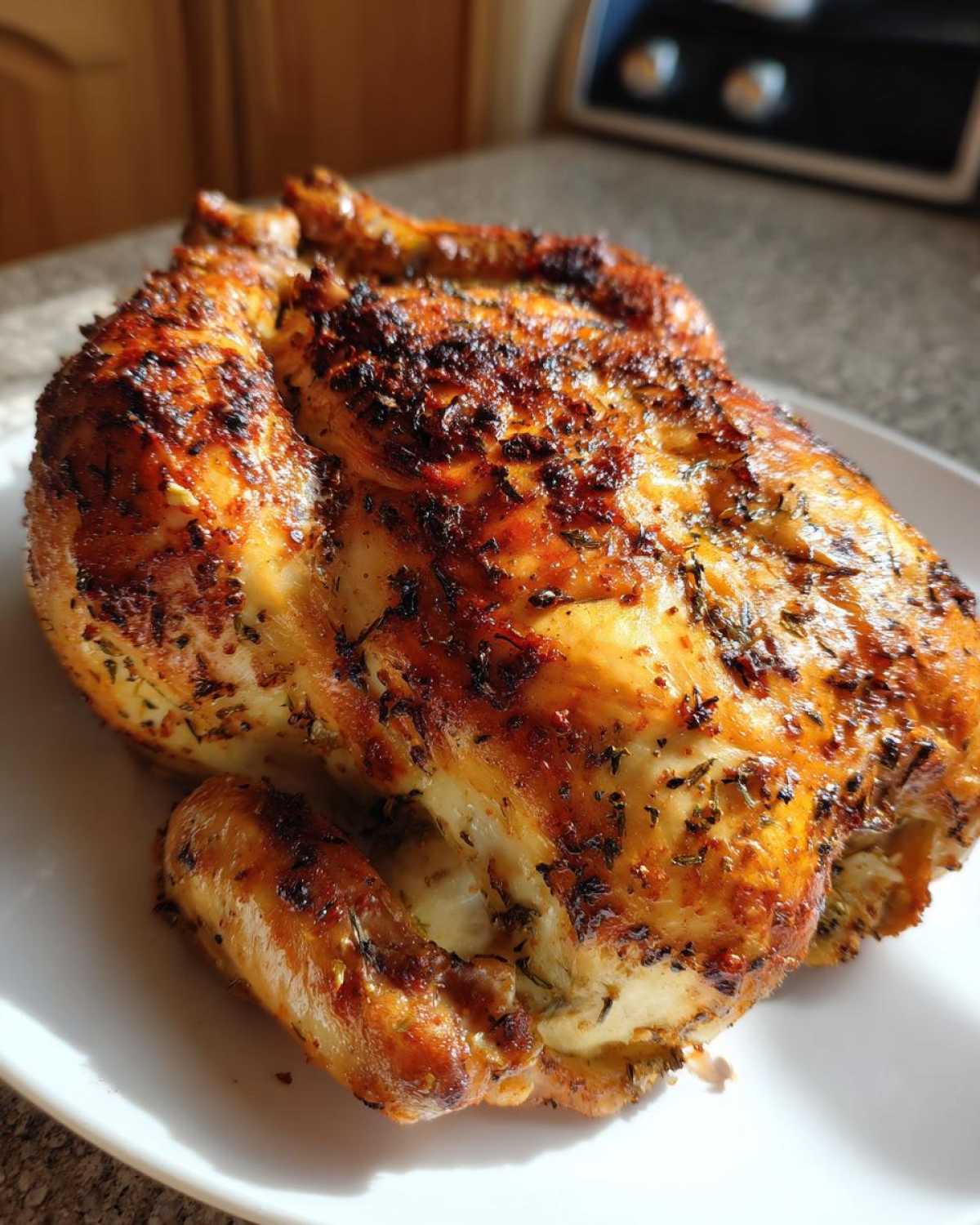 A perfectly cooked, crispy-skinned air fryer whole chicken seasoned with herbs, resting on a white plate.