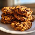 A tempting stack of golden brown breakfast cookie loaded with visible oats and chocolate chips on a white plate.