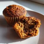 Close-up of two delicious bran muffins, one whole and one halved showing the moist interior and raisins.