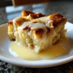 Close-up of a serving of amazing bread pudding drenched in rich vanilla sauce on a white plate.