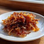 A small pile of deeply browned, glossy caramelized onions served on a white saucer.