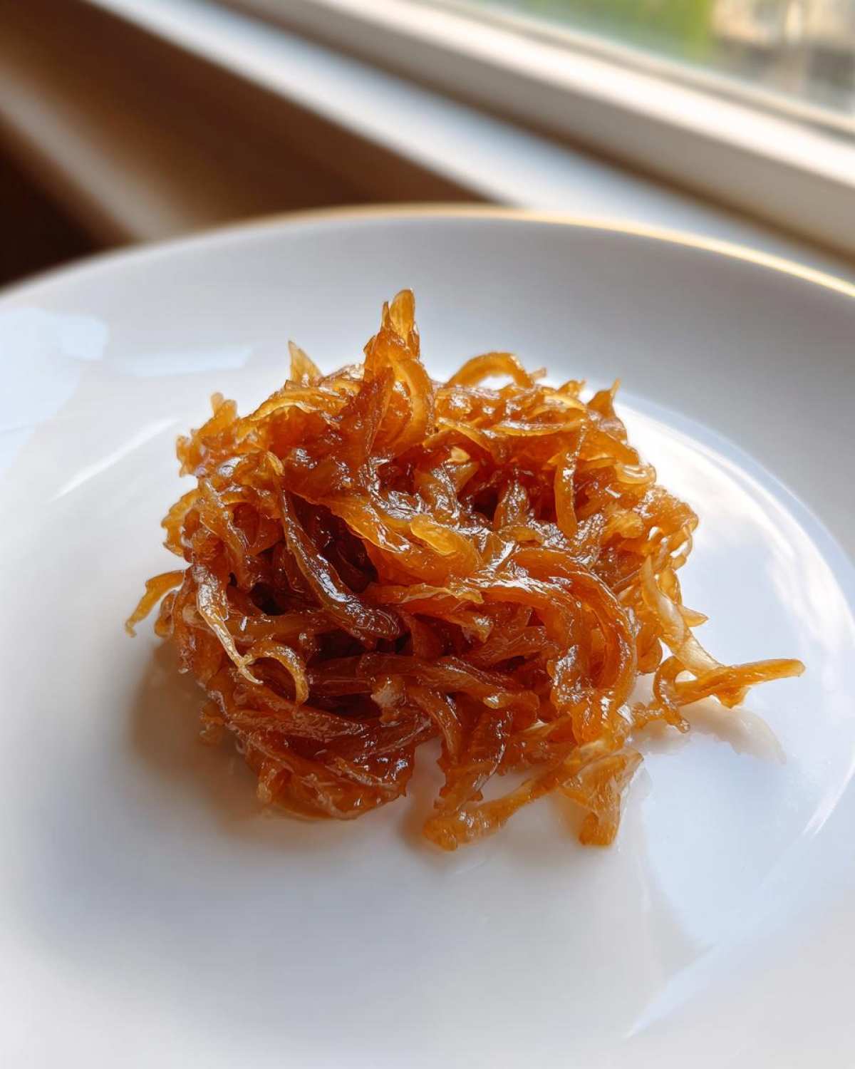 A mound of deeply browned, glossy caramelized onions served on a clean white plate.