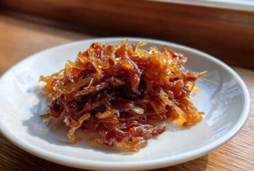 A small pile of deeply browned, glossy caramelized onions served on a white saucer.
